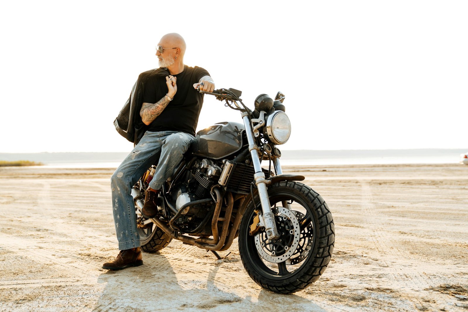 Bold senior man with tattoo posing on motorcycle outdoors